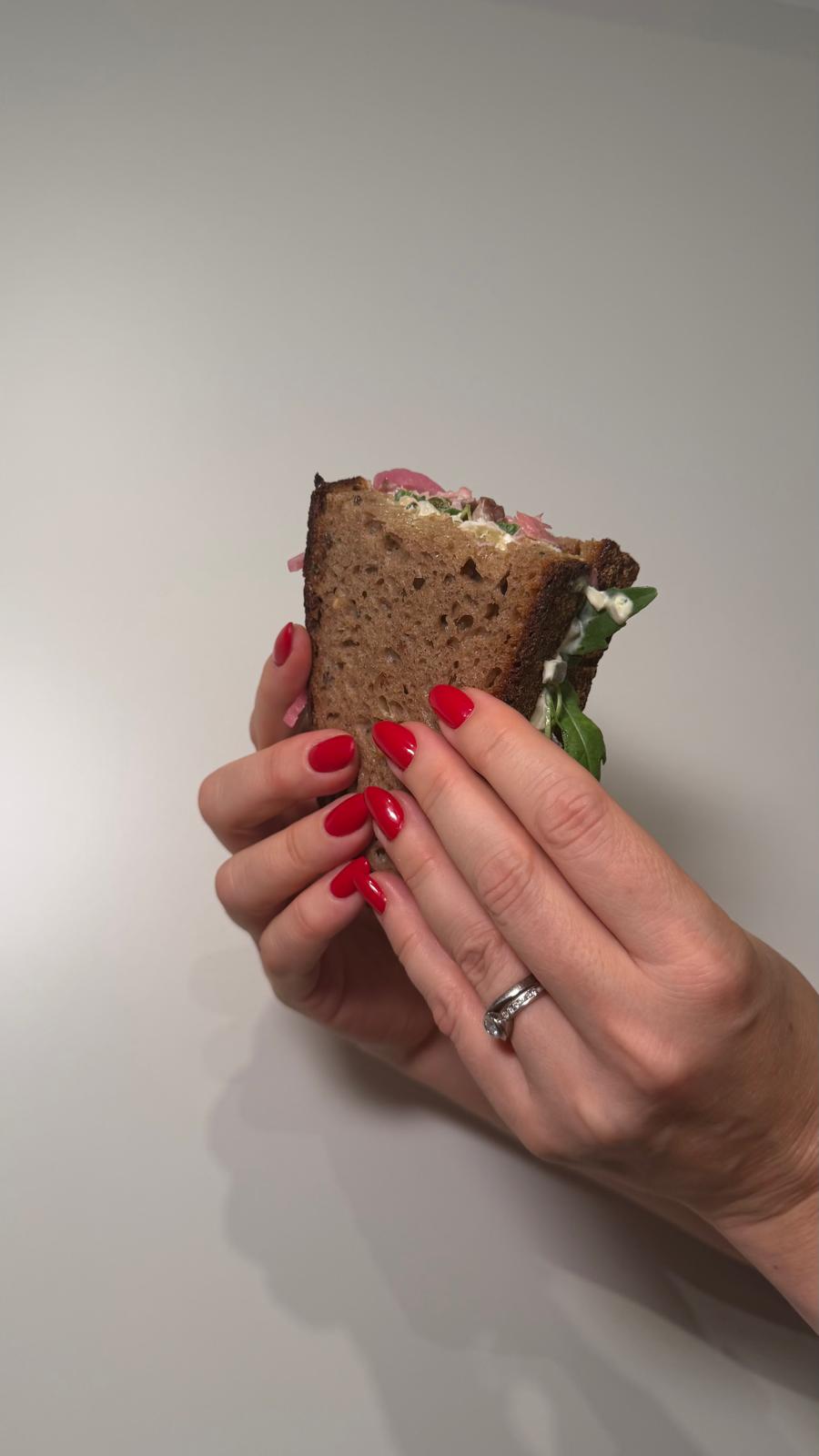 Hand hält ein aufgeschnittenes belegtes Dinkel-Sauerteigbrot